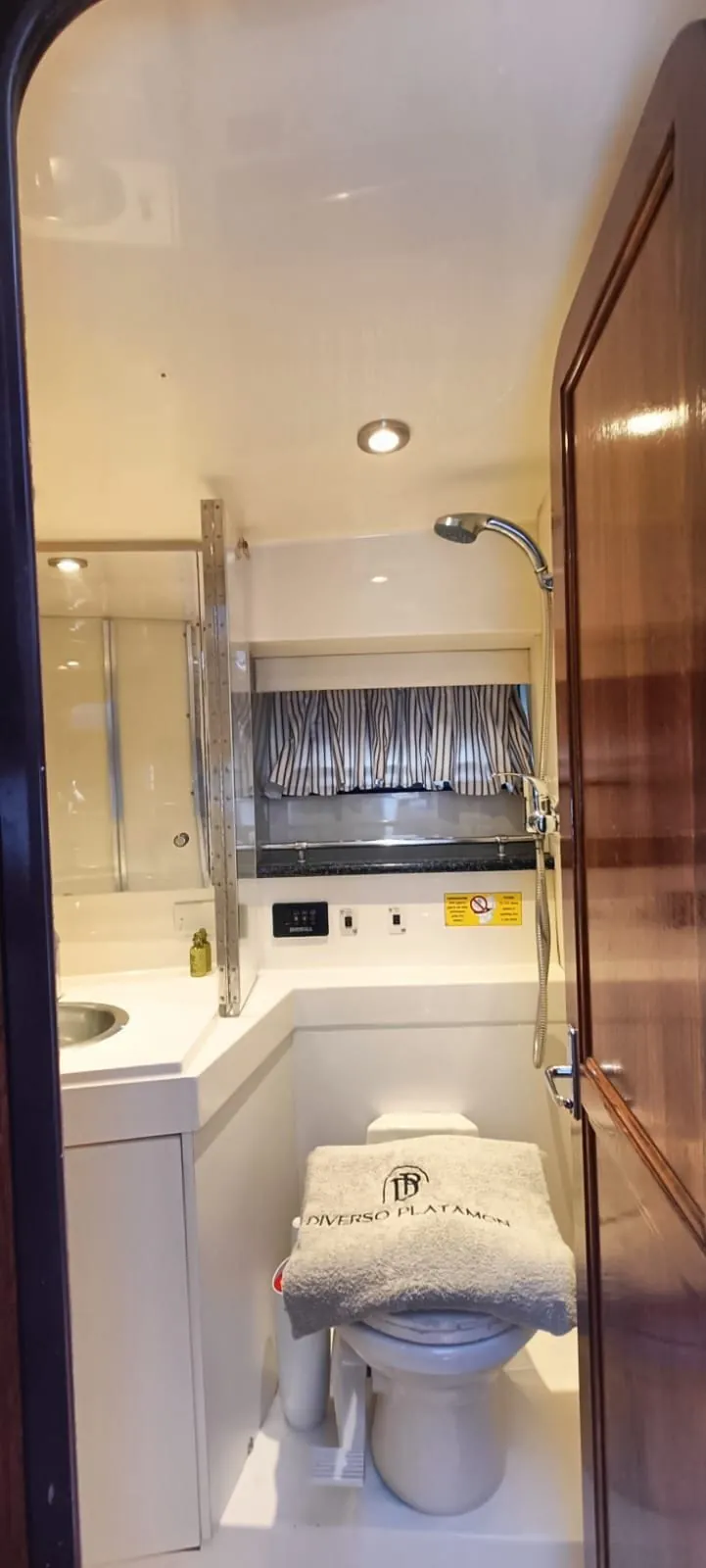 A compact ensuite head with basin, mirror and overhead shower, a towel folded on the lid