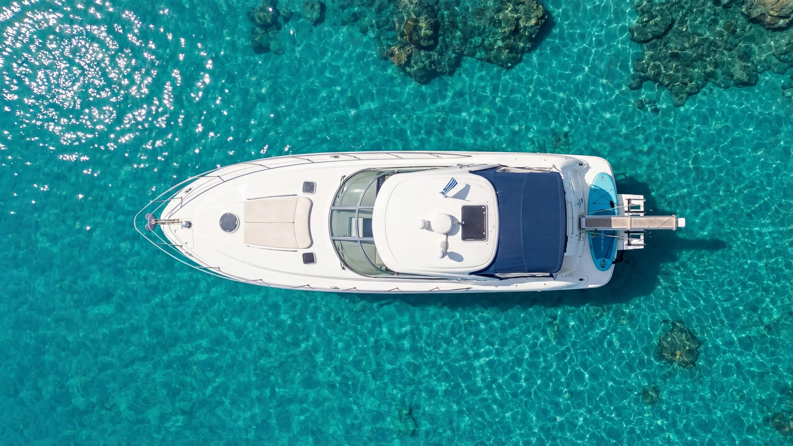 A motor yacht at anchor over clear turquoise shallows, seen from directly above